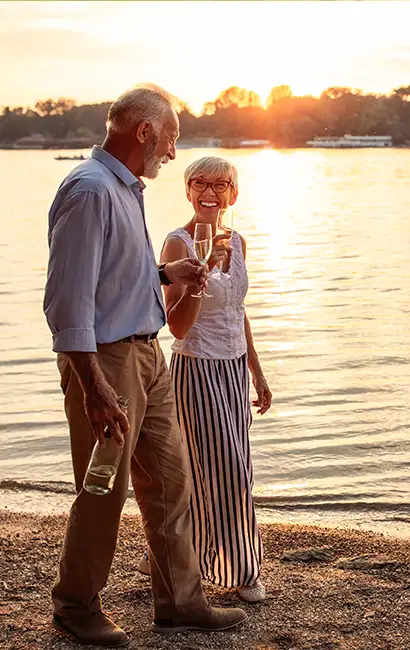 happy couple smiling while walking the beach with wine retirement strategies